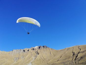 Low angle view of person paragliding against clear blue sky