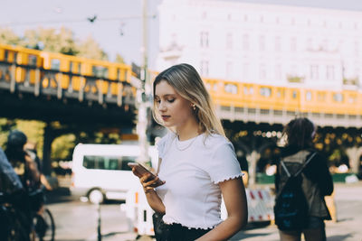 Young woman using mobile phone while walking by street in city