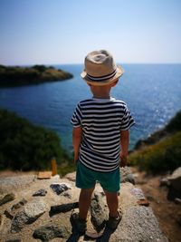 Rear view of boy standing on rock at beach