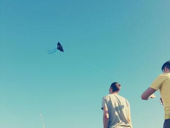 Low angle view of friends flying kite against clear blue sky