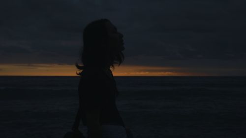 Silhouette woman standing at beach against sky during sunset