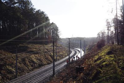 Railroad tracks by road in forest against sky