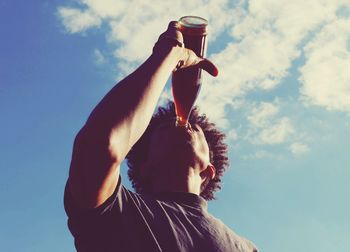 Low angle view of man drinking cola against sky