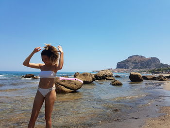 Rear view of woman on rock at beach against clear sky