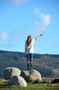 Rear view of woman standing on rock against sky