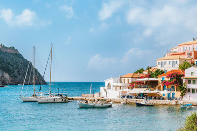 Sailboats in sea by buildings against sky