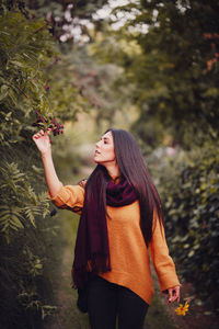 Young woman standing by tree against plants