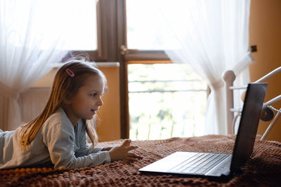 Child watching cartoons on laptop. serious kid with technology at home on bed spending time on-line