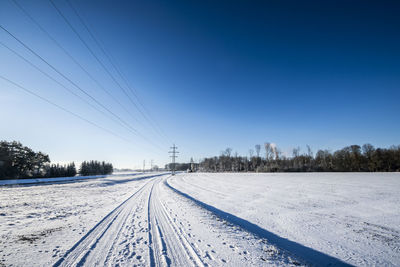 Railway tracks on snow covered field against clear blue sky