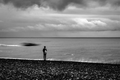 Rear view of man standing at beach against sky