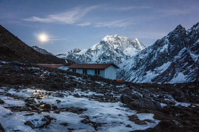 Snow covered house by mountain against sky during winter