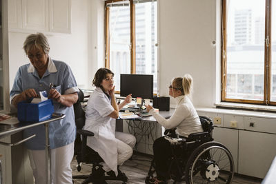 Female medical expert talking with disabled patient while senior nurse working