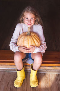 A beautiful cheerful girl sits on a doorstep of a house, holding a large orange pumpkin. halloween