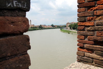 Close-up of brick wall with river and town against sky