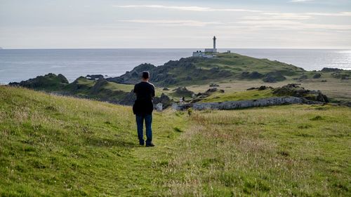Rear view of man standing on field by sea against sky