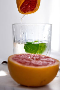 Close-up of grapefruit squeezing in glass over white background