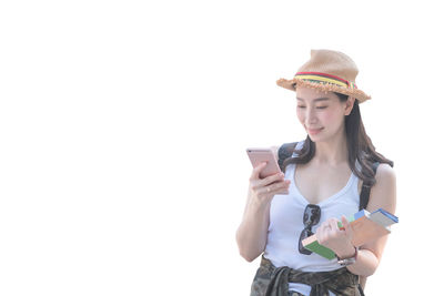 Young woman using phone while standing against white background