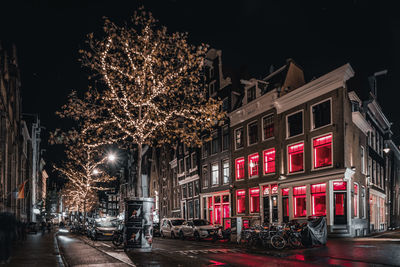 Illuminated street by buildings in city at night