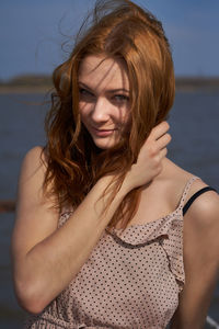 Smiling young red haired woman fixes her hair. outdoor portrait of young attractive woman.