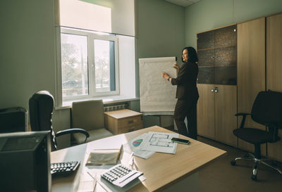 Happy businesswoman in office. female tutor, coach in front of board. diagrams  on the table