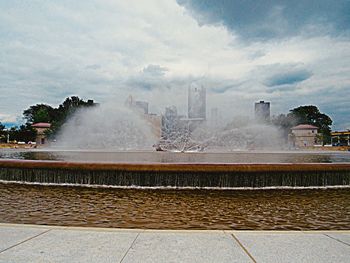 View of fountain in city against cloudy sky