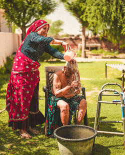 Daughter bathing her old mother in yard