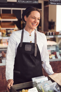 Happy female owner looking away while standing in grocery store