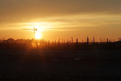 Silhouette wooden posts on field against orange sky