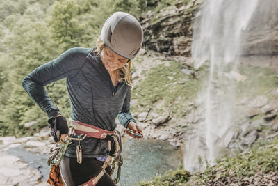 Woman puts gear back on harness after rappelling waterfall in catskill