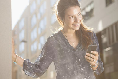 Smiling young woman using mobile phone while standing outdoors