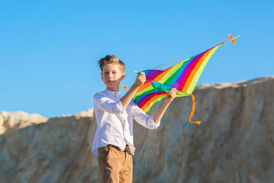 A handsome boy in a white shirt with a multicolored kite on blue sky background.