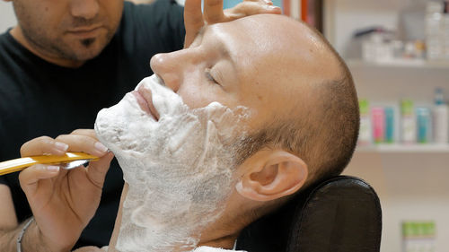 Midsection of barber doing shaving of mature man in salon