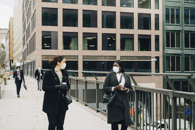 Female colleagues talking with each other while walking on bridge in city