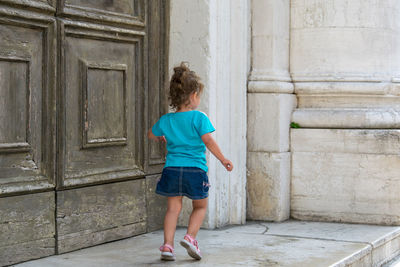 Rear view of girl walking by closed wooden door