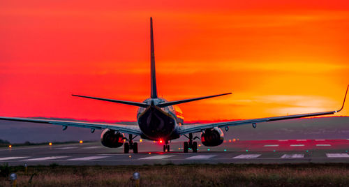Airplane at airport runway against sky during sunset
