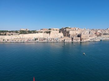 Buildings by sea against clear blue sky