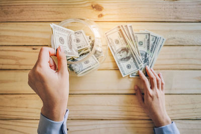 Cropped hand putting paper currency in jar over table