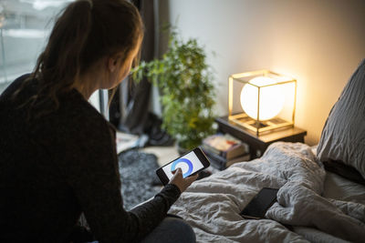 Woman holding mobile phone while sitting on bed