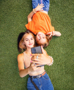 Two girls lie on the grass take a selfie and laugh, social networks, younger and older sister,