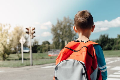 Rear view of schoolboy carrying backpack while standing on road