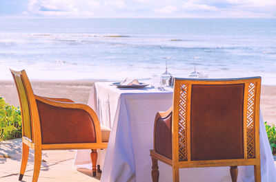 Empty chairs and tables on beach against sky