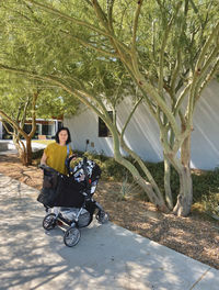 Portrait of woman standing with baby stroller on footpath