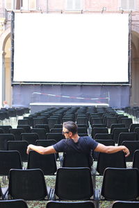 Rear view of man sitting against projection screen on chair