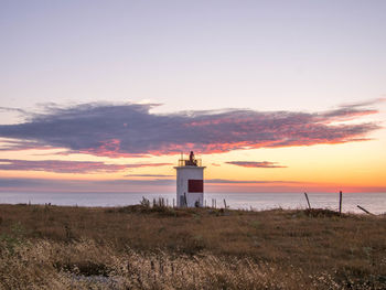 Lighthouse on beach against sky during sunset