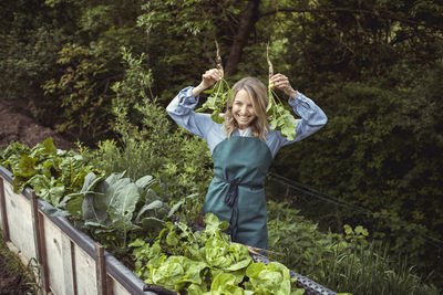 Full length portrait of smiling young woman standing against plants