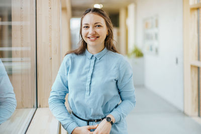 Portrait of happy young businesswoman standing at office corridor