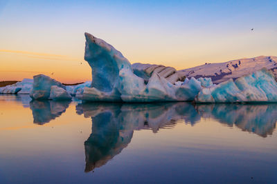 Scenic view of icebergs in sea against snowcapped mountains and sky during sunset