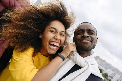 Happy young woman pulling cheek of friend outdoors