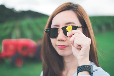 Close-up portrait of young woman in sunglasses holding yellow flower