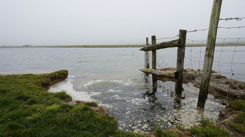 Wooden posts in sea against clear sky